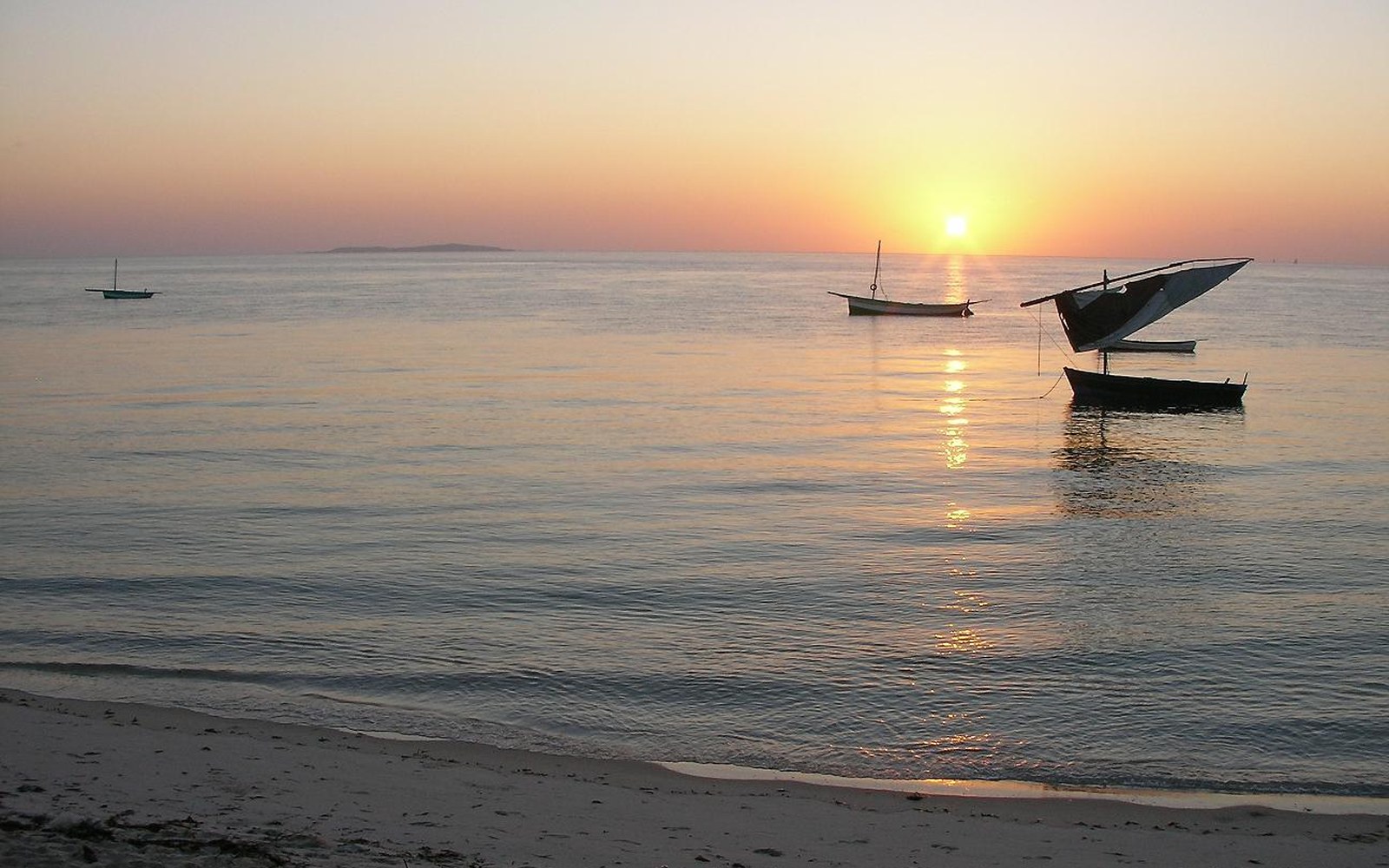 Small boats and one rigged dhow at anchor in shallow water at sunset