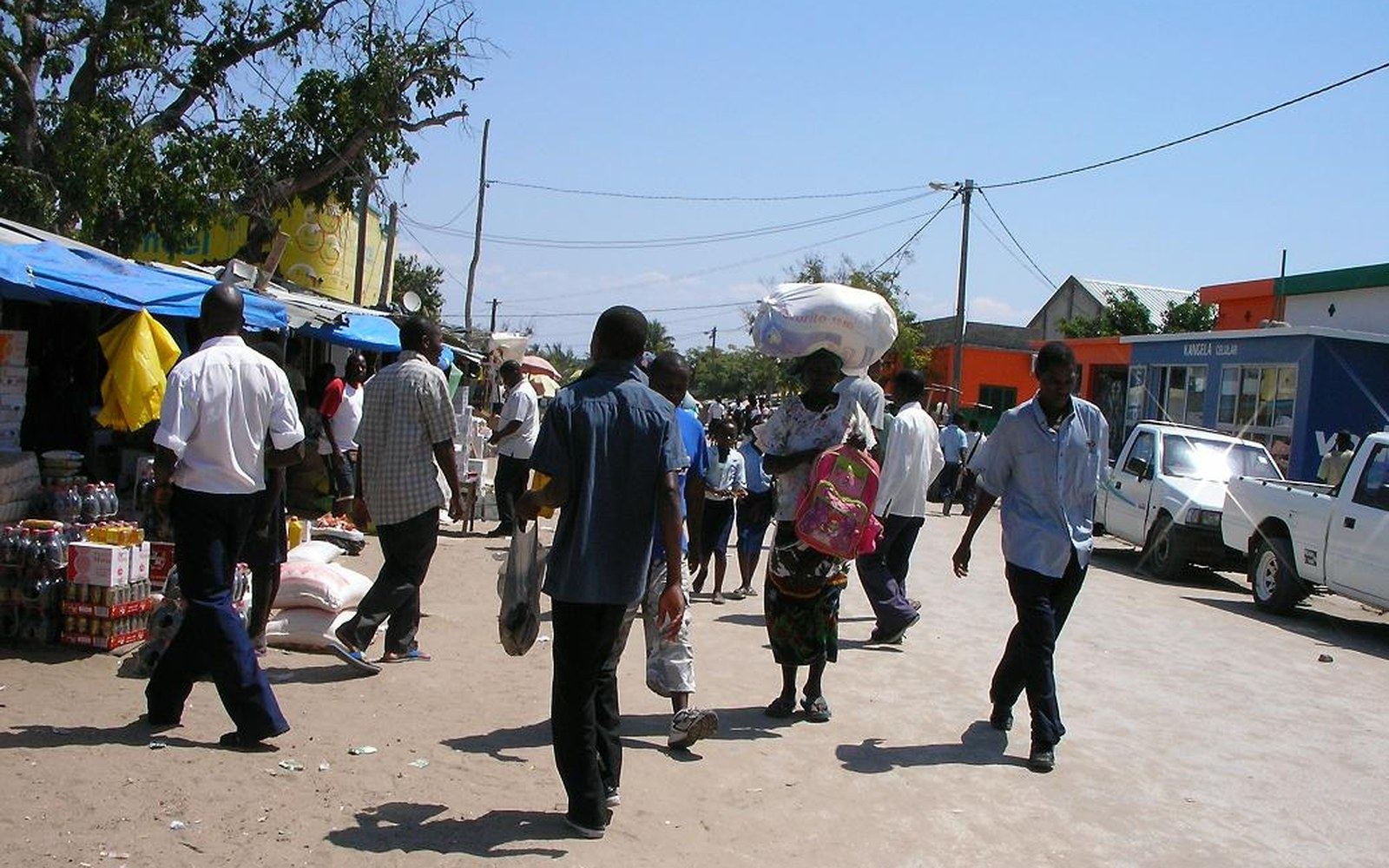 A busy sand street of market stalls with people carrying goods on their heads