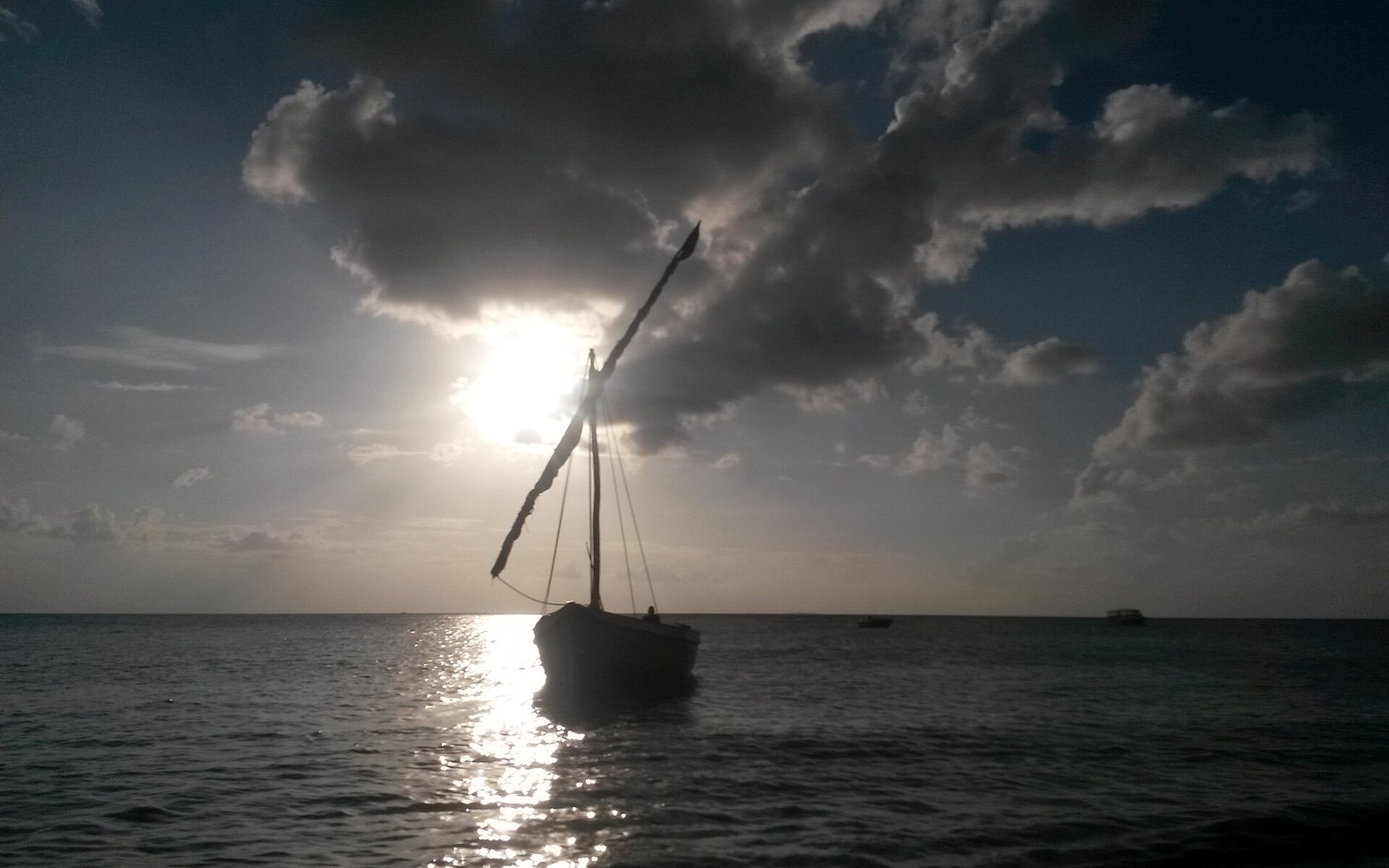A dhow moored in calm water at dusk, its yard raised and sail furled